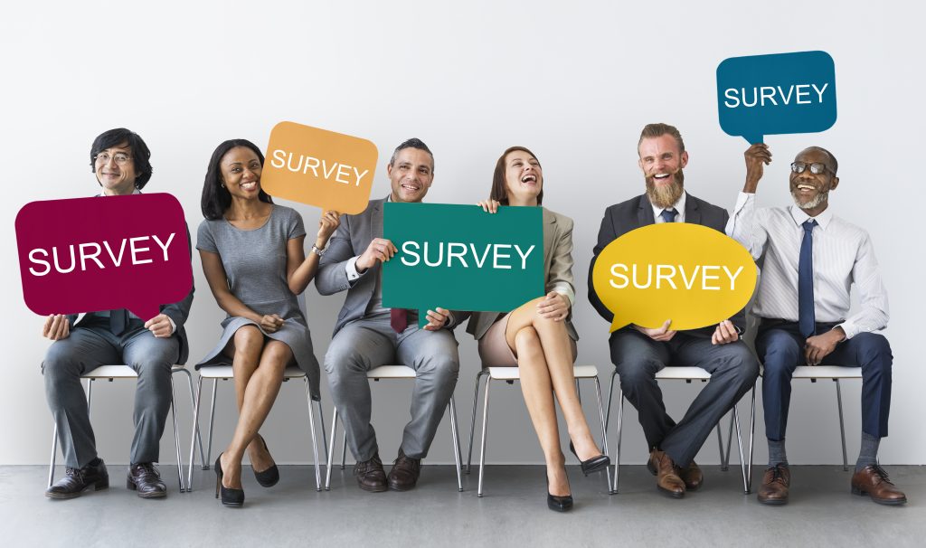 sześć osób siedzących na krzesłach trzymających w rękach tablice z napisami "survey"